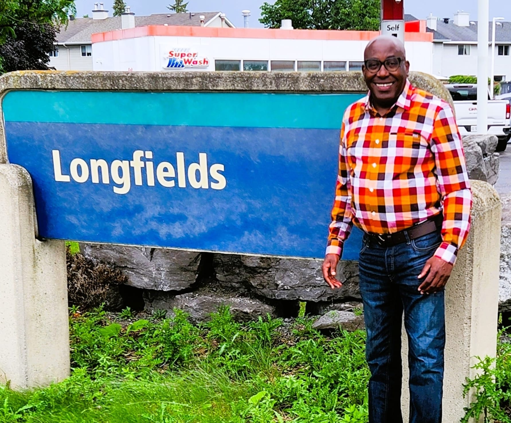 Jules Ruhinda standing beside the Longfields sign